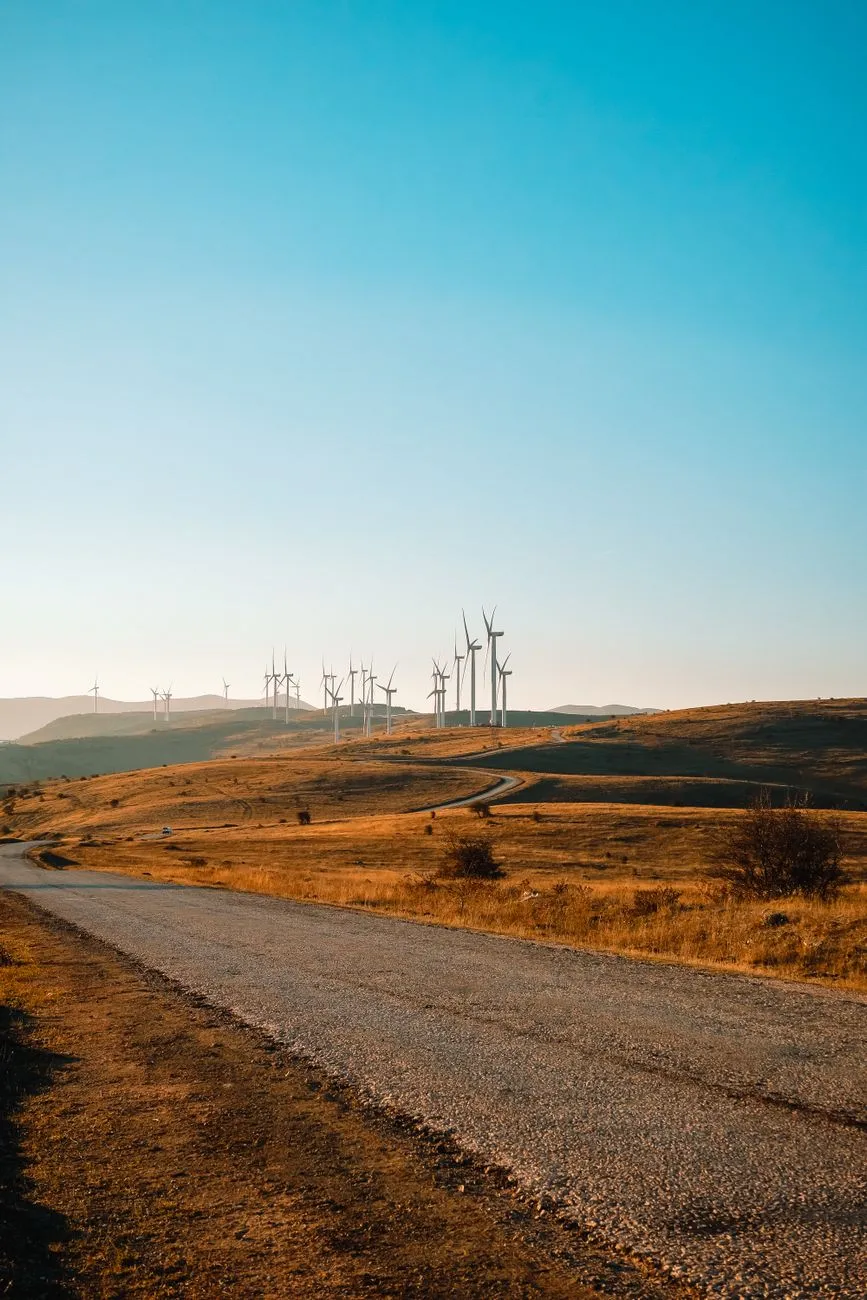 Gravel road through golden hills toward a row of wind turbines